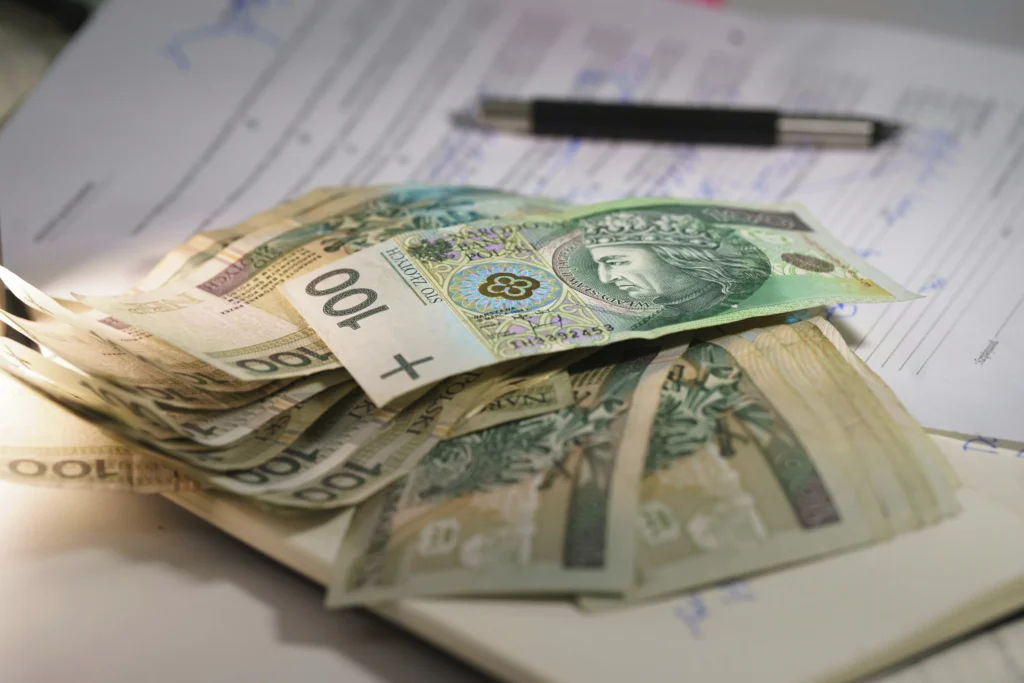 Stos polskich banknotów o nominale 100 złotych na biurku z dokumentami i długopisem.
